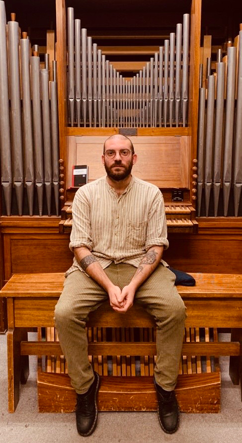 Portrait of Ivano Pecorini seated in front of an organ.